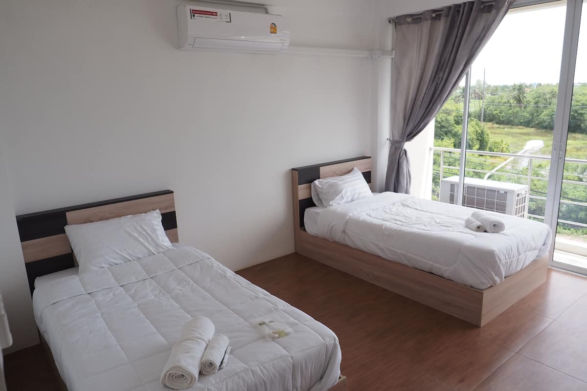 Habitación de hotel con dos camas, un ventanal con vistas a zonas verdes y un equipo de aire acondicionado en la pared.