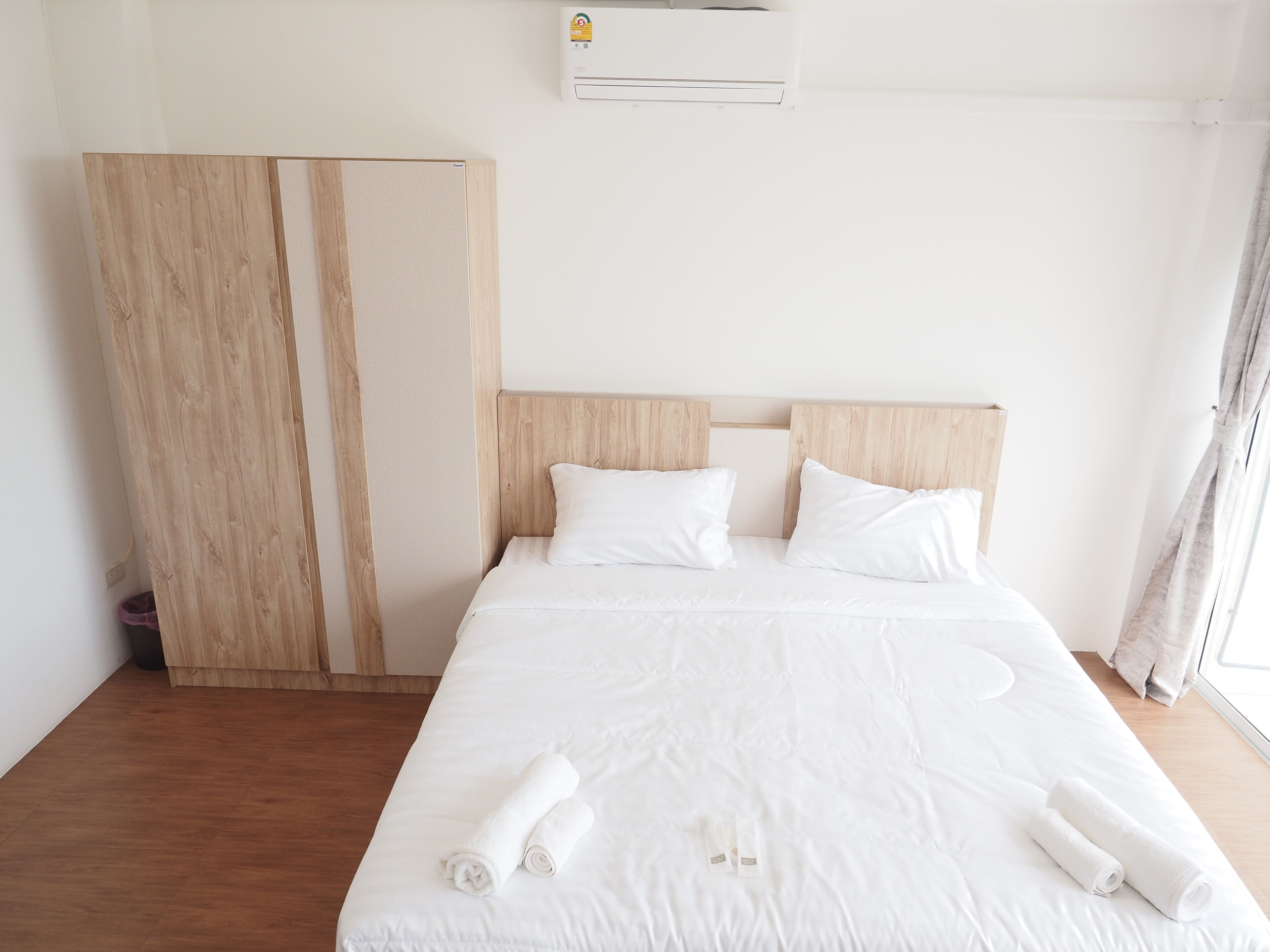 Habitación de hotel con cabecera de madera, ropa de cama blanca y dos toallas enrolladas sobre la cama.