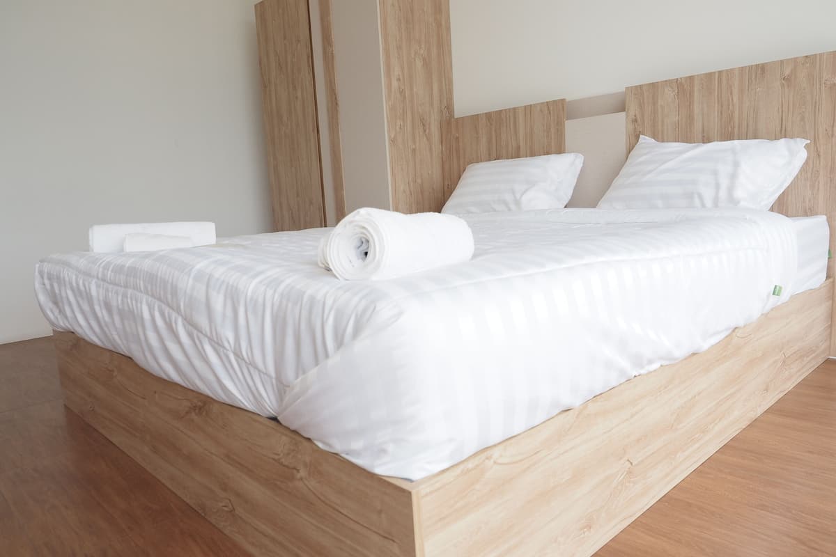 Una cama de madera con ropa de cama y almohadas blancas.