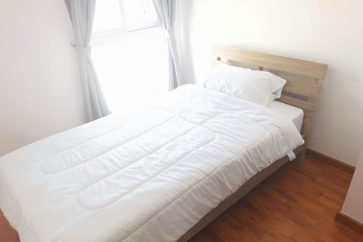 Una cama bien hecha con cabecera de madera en una habitación con suelo de madera y paredes blancas.