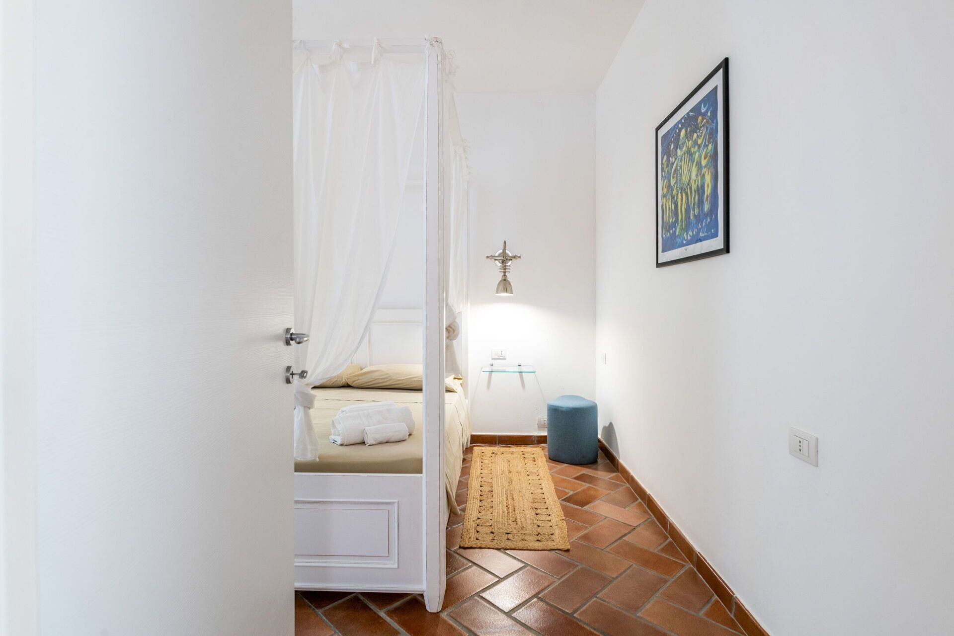 Quarto com cama, mesa de cabeceira, abajur, tapete e quadro na parede.