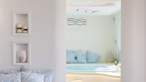 Un espace de détente moderne avec un coin salon aux lignes courbes, une fontaine murale et une vue sur l’océan.