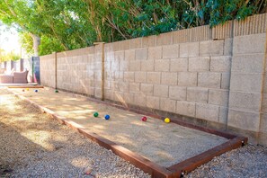 A courtyard with a long, narrow, rectangular gravel area bordered by a brick wall, surrounded by trees. - The Cactus Rose: Heated Pool, Putterball & Bocce! (Glendale)