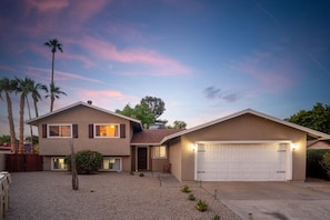 A two-story house with a garage, a driveway, and a small front yard with a tree and shrubs.