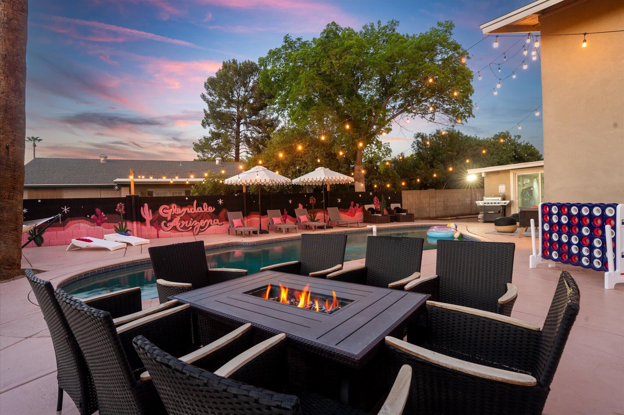 A poolside area with lounge chairs, a fire pit table, and string lights.