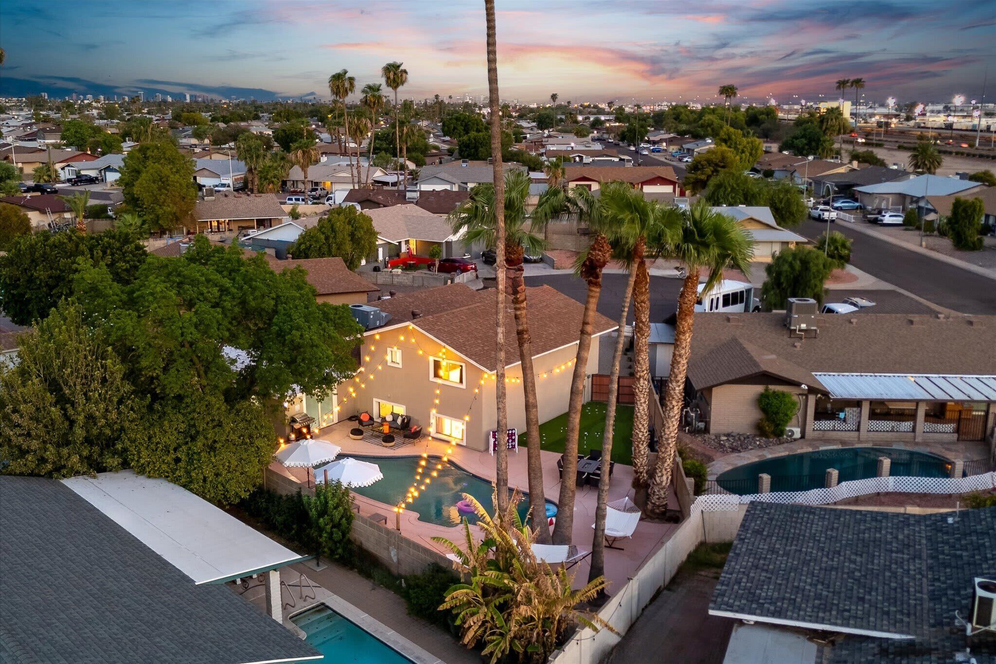 A residential area with a house featuring a swimming pool, palm trees, and a view of the cityscape.