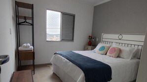 Een slaapkamer met een bed, een bureau, een hangende garderobe, een raam en een plafondventilator.