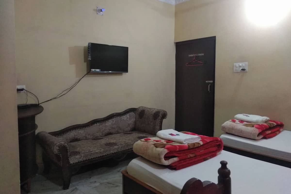 Una habitación con sofá, dos camas, televisión instalada en la pared y una puerta con perchero.