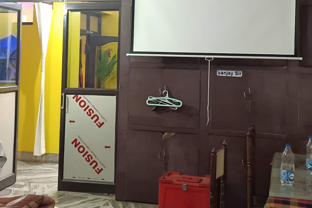 Una habitación con proyector, una pizarra, un armario y un caja roja para guardar objetos.