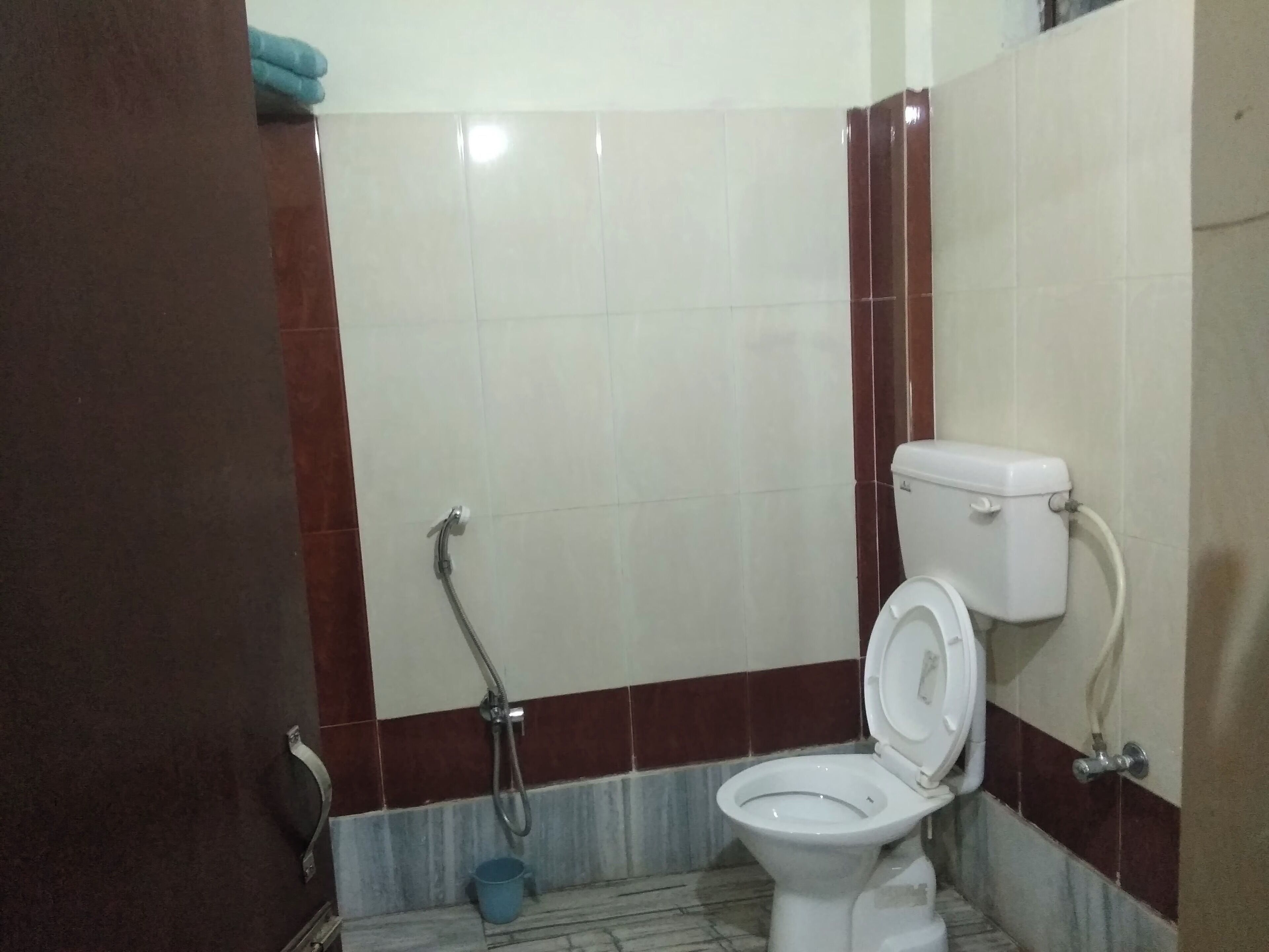 A bathroom with a toilet, a shower, and a blue bucket on the floor.