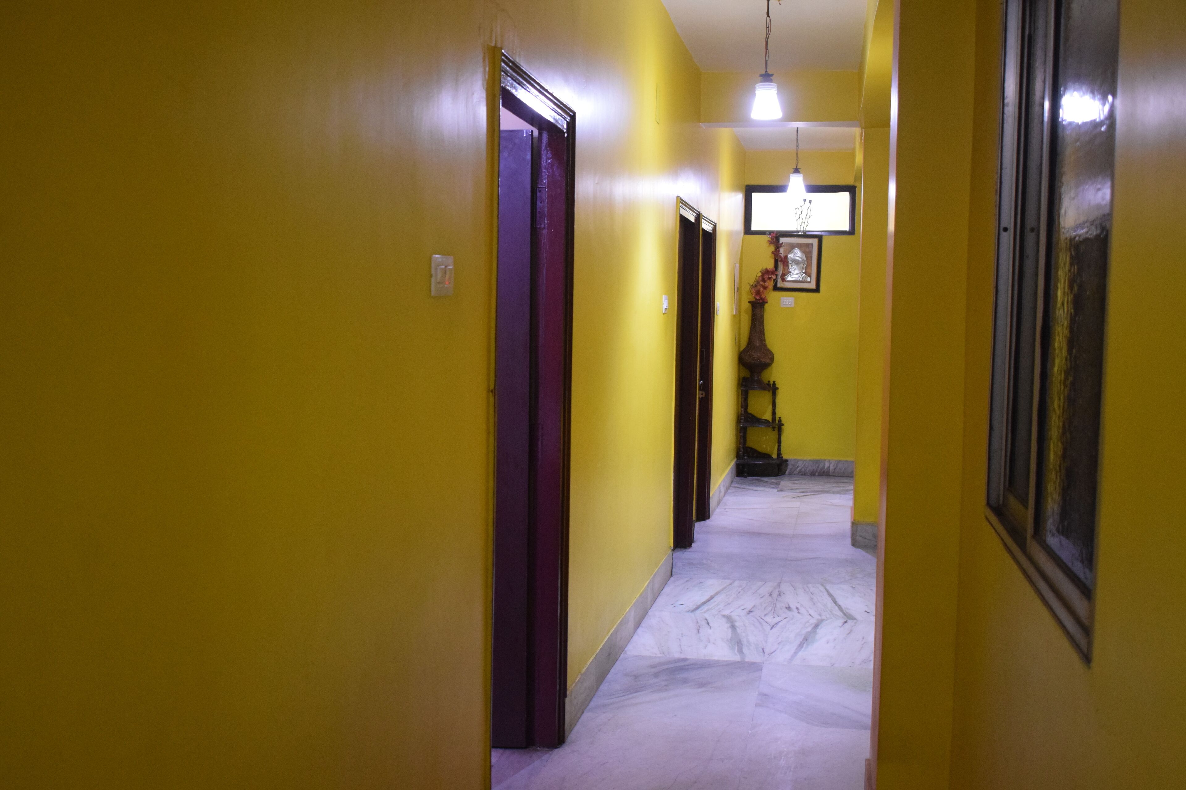 Un passadís amb parets grogues i un sòl de marbre que condueix a una porta al final.