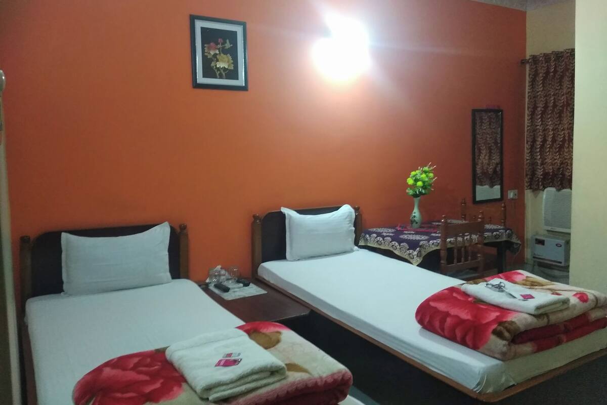 Una habitación de hotel con dos camas individuales, una mesita con un florero y un espejo en la pared.