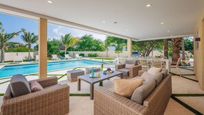 A covered outdoor area with a pool, wicker furniture, and a barbecue grill.