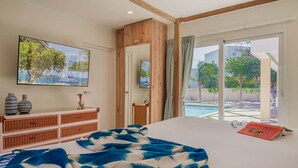 A bedroom with a large bed, a wooden dresser, a TV, and a view of a swimming pool.