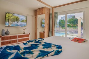 Une chambre avec un grand lit, une commode en bois, une télévision et une vue sur une piscine.