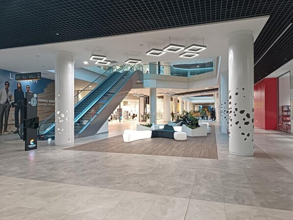Shop and dine in style in this modern shopping mall's central open area, featuring a contemporary seating arrangement and a prominent escalator.