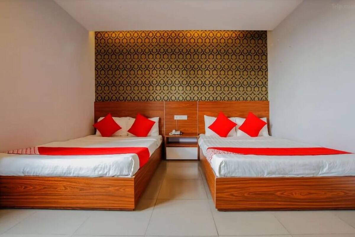 A hotel room with two wooden beds, each with red and white bedding, and a patterned wall behind the beds.