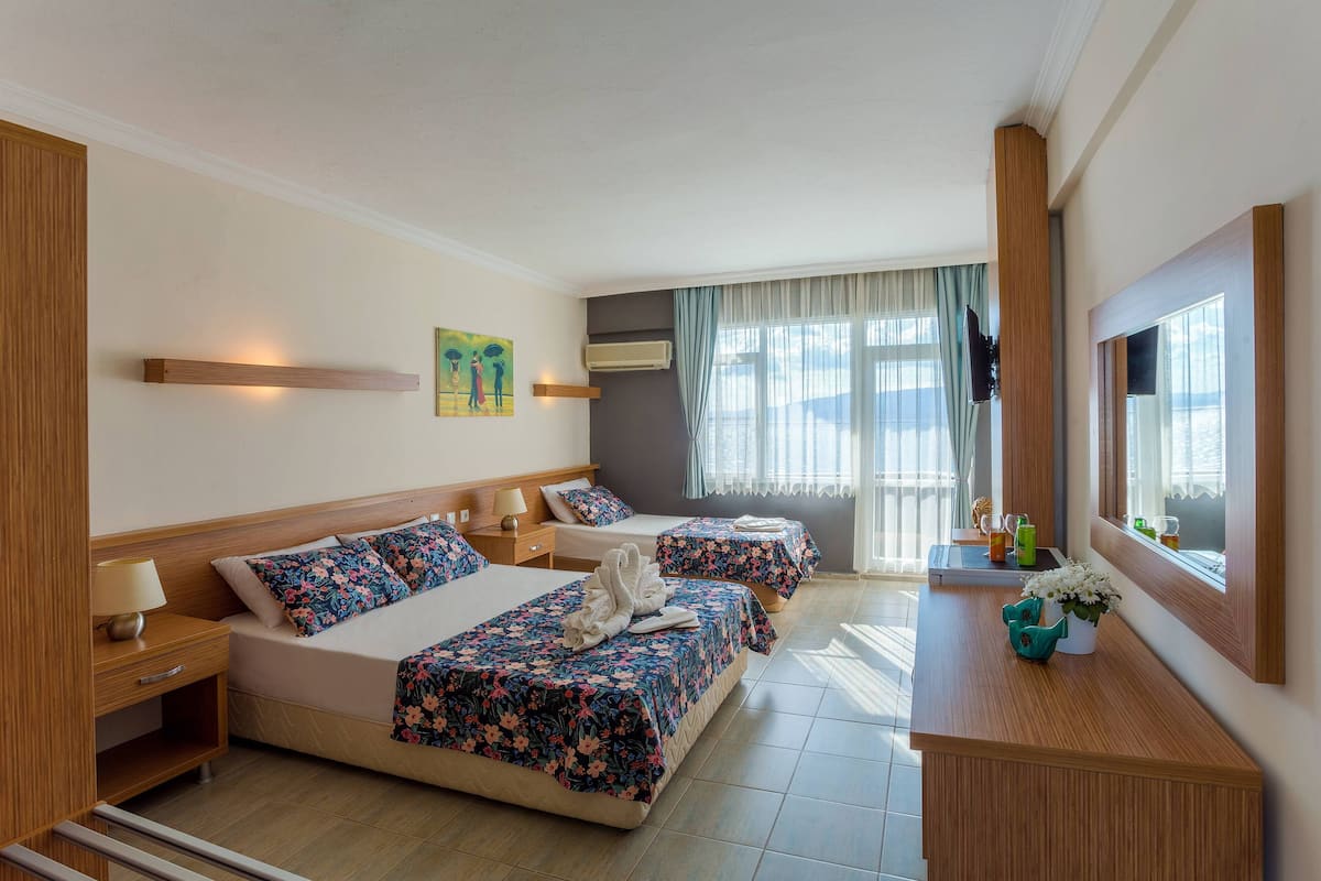 A hotel room with two beds, a TV, a desk with a mirror, and a window with curtains.