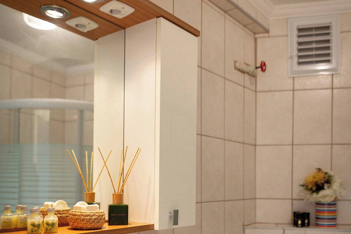 Un baño con lavamanos blanco, espejo y repisa con artículos de aseo.