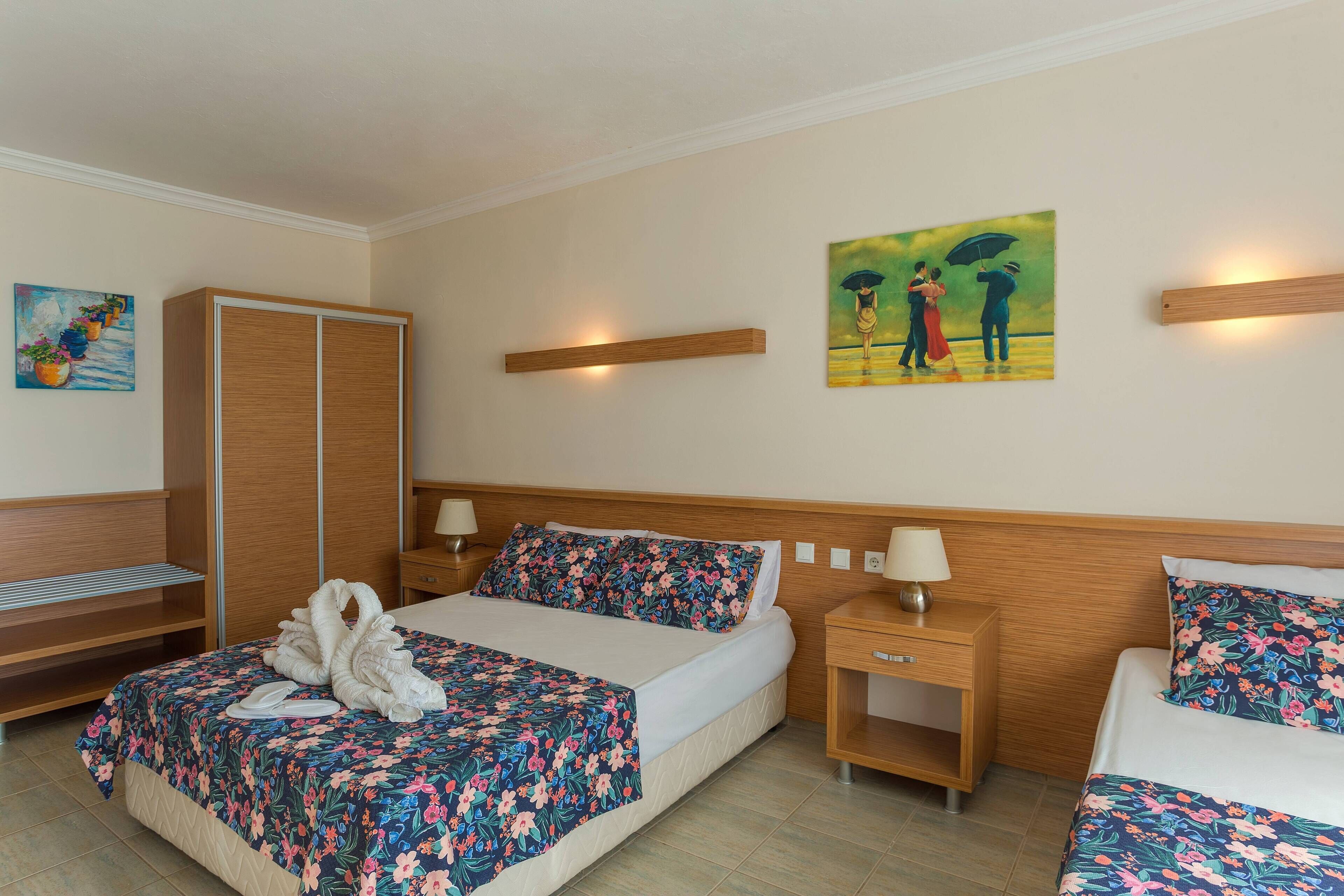 A hotel room with a bed, a wardrobe, a nightstand, and a painting on the wall.