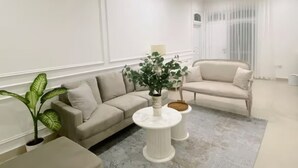 En moderne stue med en beige sofa, et lille rundt sofabord og en potteplante.