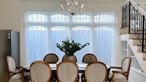 En spisestue med lysekrone, store vinduer og en trappe.