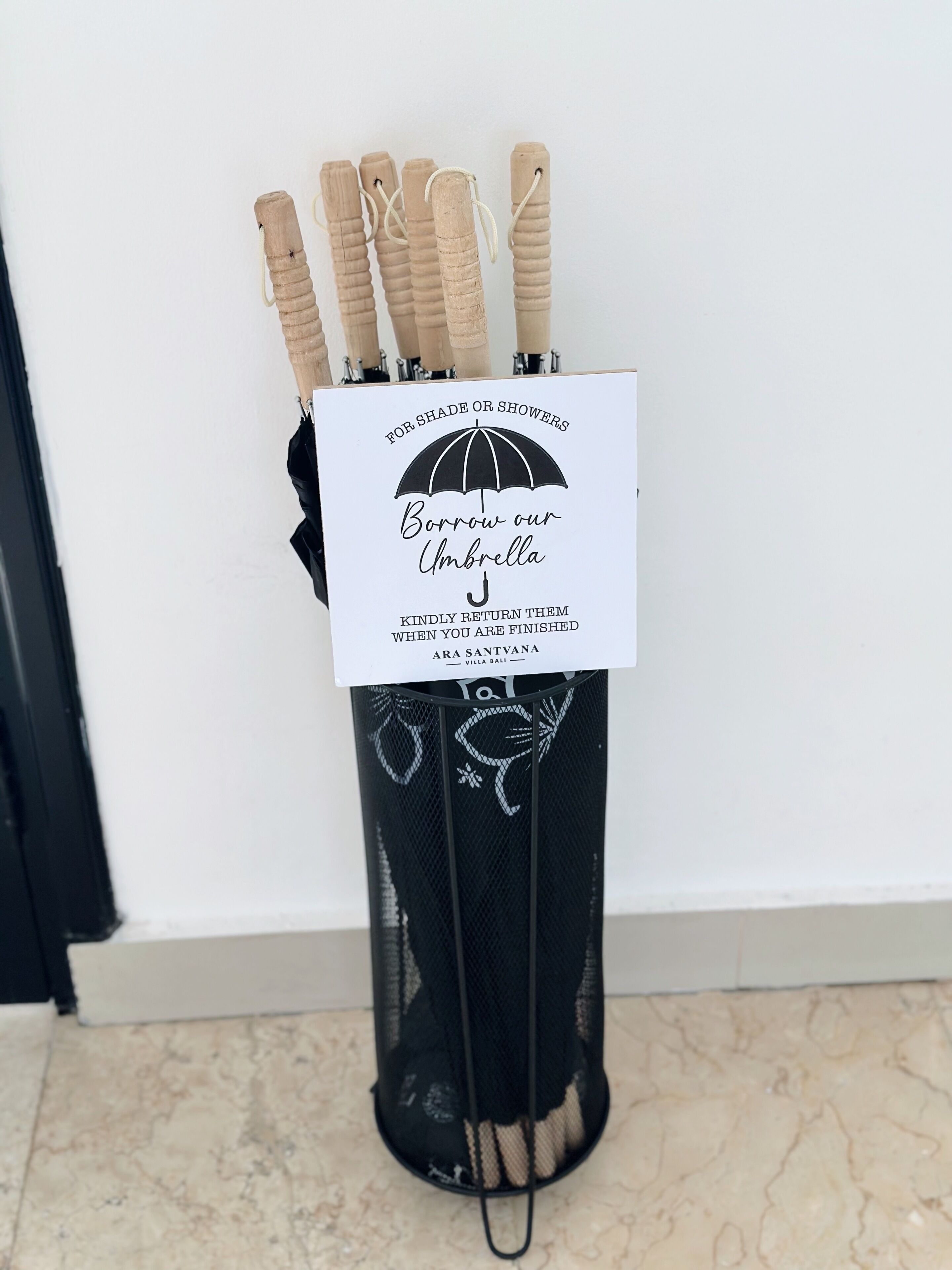 Un portariviste con ombrelli dalle maniglie in legno e un cartello pubblicitario per il noleggio di ombrelli.