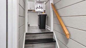 A narrow staircase with wooden steps and a wooden handrail, leading to a kitchen area with cabinets and a trash can. - Charming Retreat w/ Pool Table in Chesterfield! (Chesterfield)