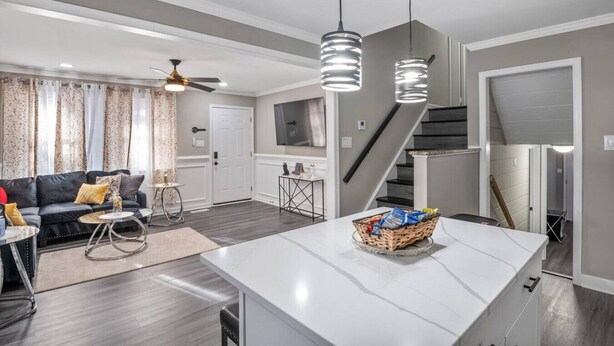 A modern kitchen with a central island, a dining area with a black leather sofa, and a staircase leading to an upper level. - Charming Retreat w/ Pool Table in Chesterfield! (Chesterfield)