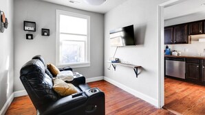 Un salon moderne avec un canapé en cuir, un téléviseur à écran plat fixé au mur et un plancher en bois.
