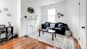 A living room with a fireplace, a black leather sofa, a coffee table, and a white rug. - Quaint Escape for 2 Near Richmond Battlefield Park (Richmond)