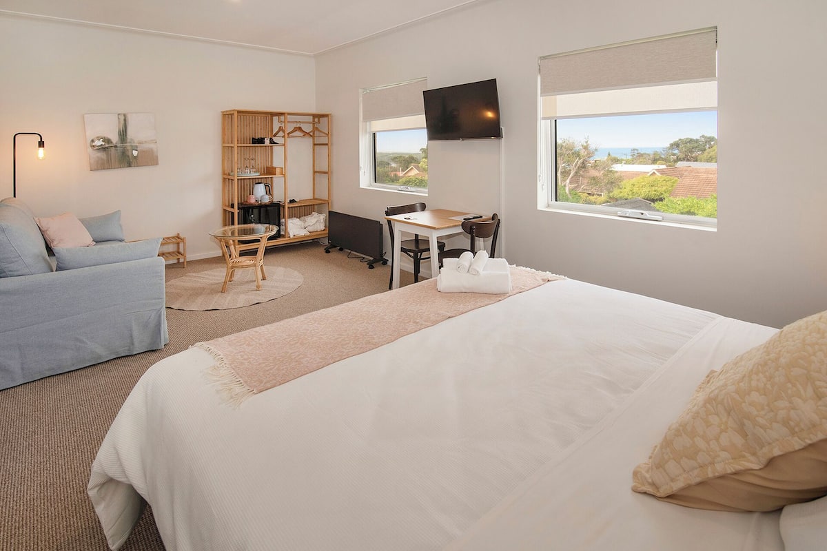 A hotel room with a bed, a desk, a chair, a wardrobe, and a TV.