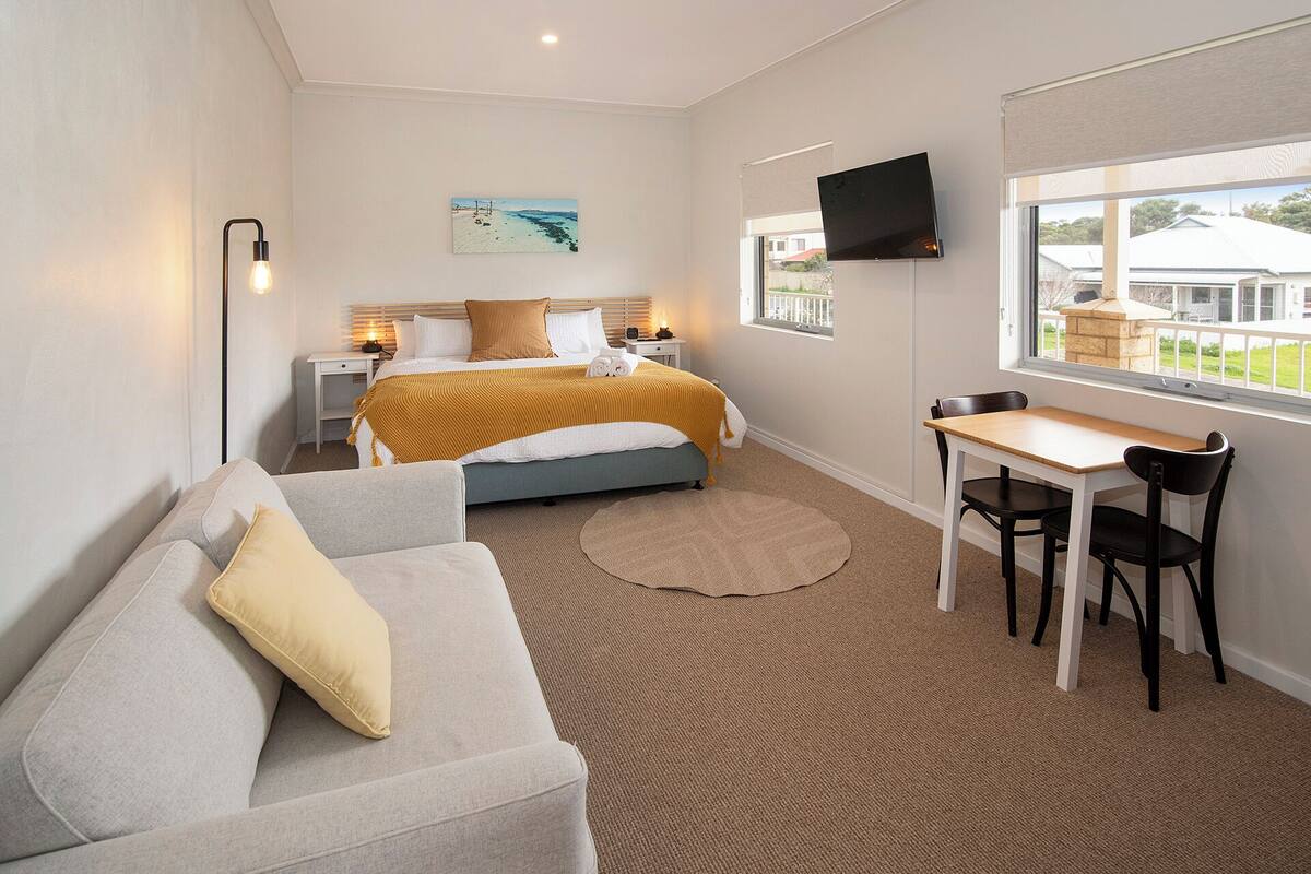 A hotel room with a bed, a sofa, a table with chairs, a TV, and a window with a view.