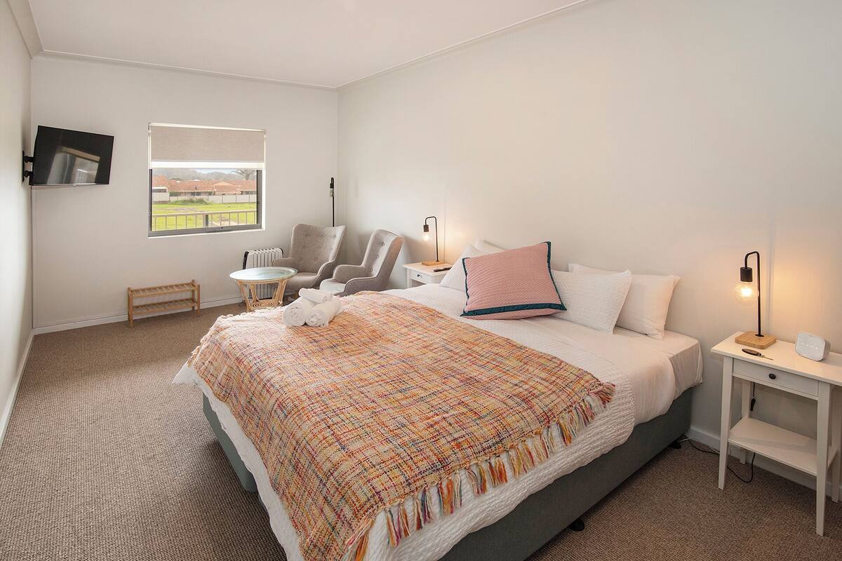 A hotel room with a large bed, a chair, a small table, a TV, and a window with a view.