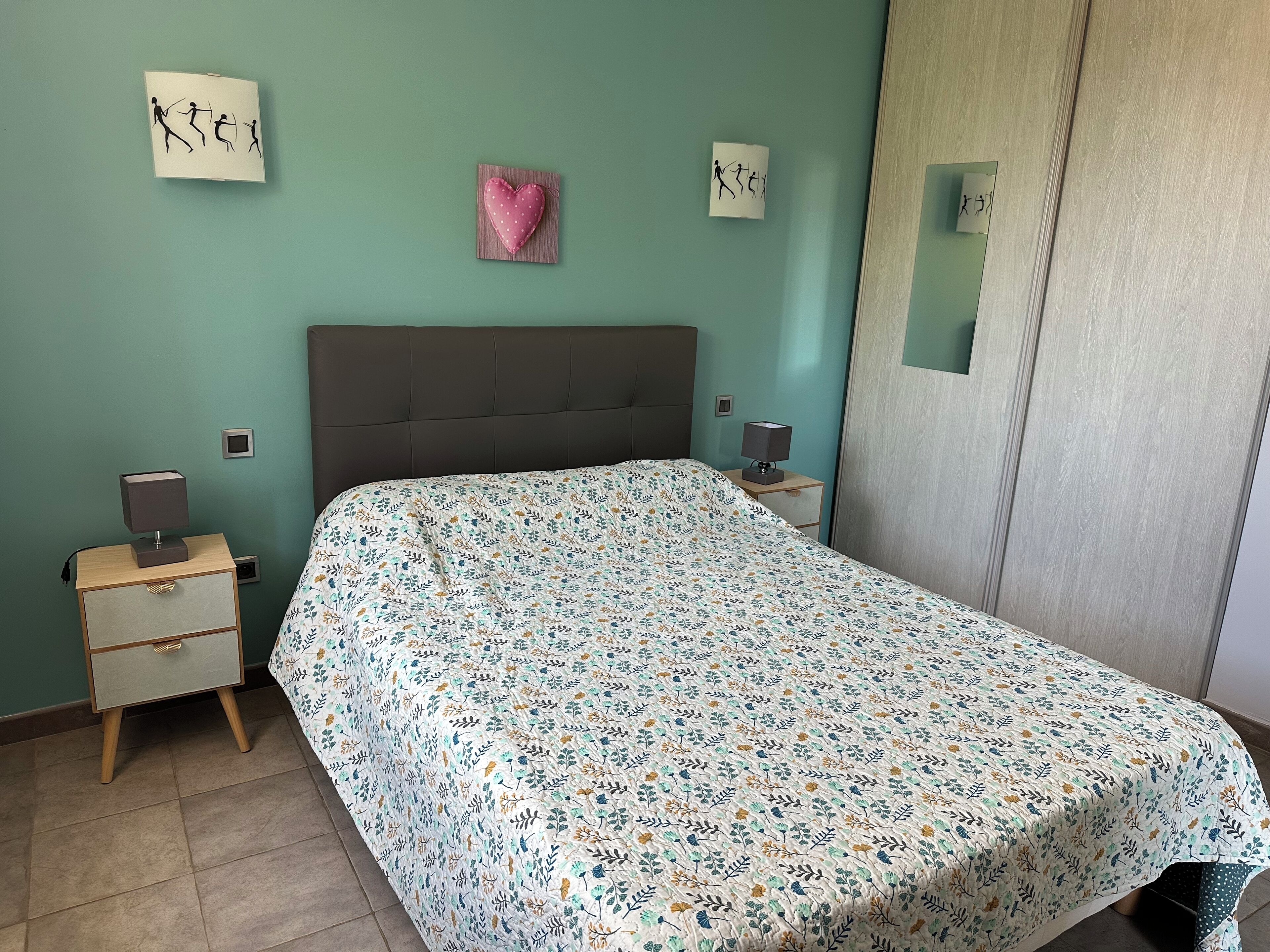 Een slaapkamer met een bed, nachtkastjes, een spiegel en wanddecoratie.