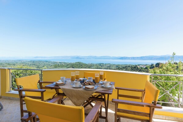 A dining table set with plates, cups, and glasses on a balcony overlooking a scenic landscape.