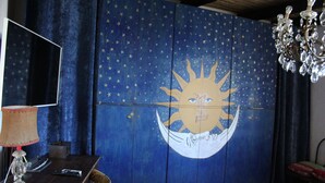 Een kamer met een muurschildering van een sterrenhemel, een houten bureau, een lamp en een kroonluchter.