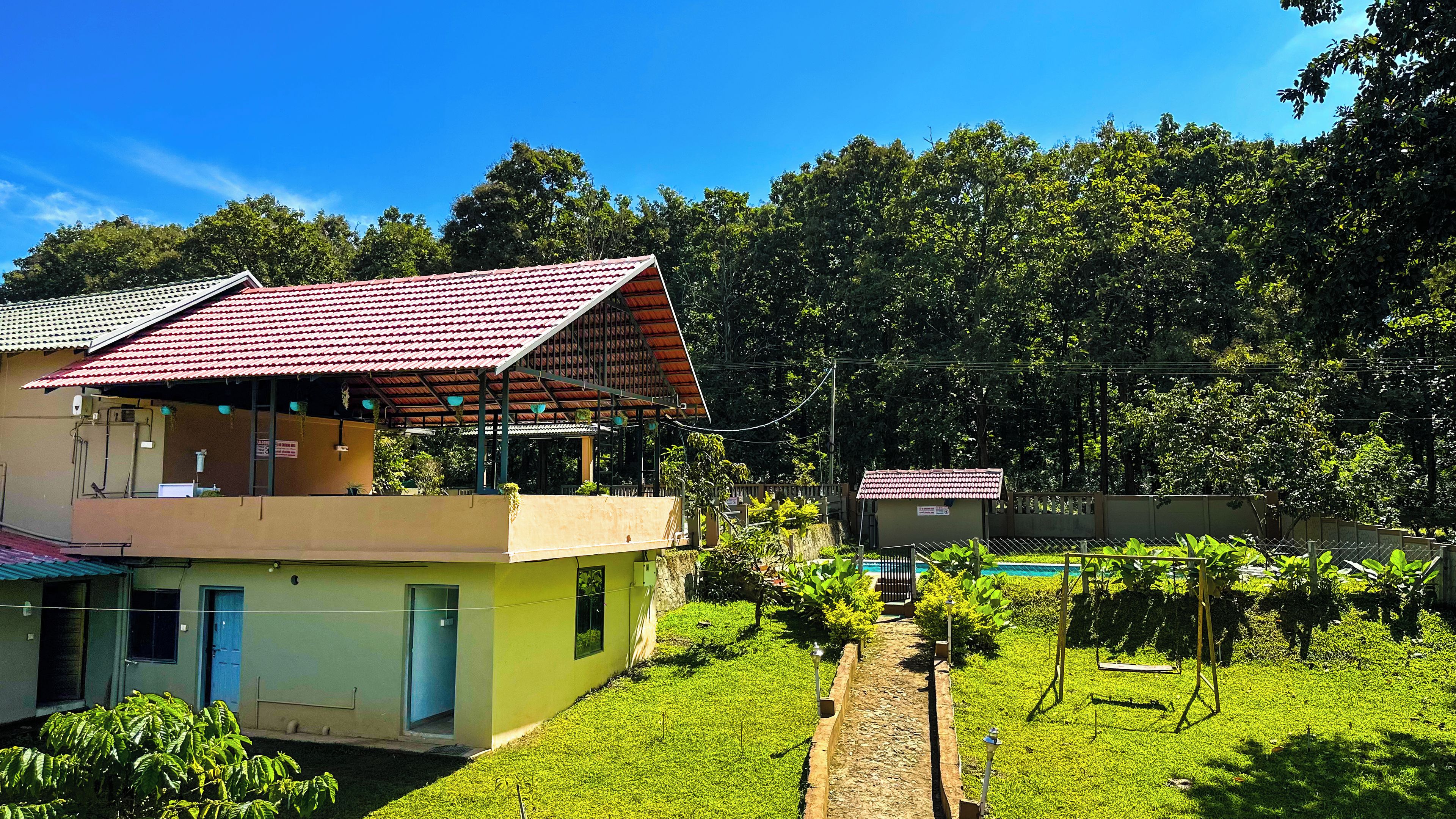 A two-story building with a red-tiled roof, a balcony, and a small pool area surrounded by greenery.