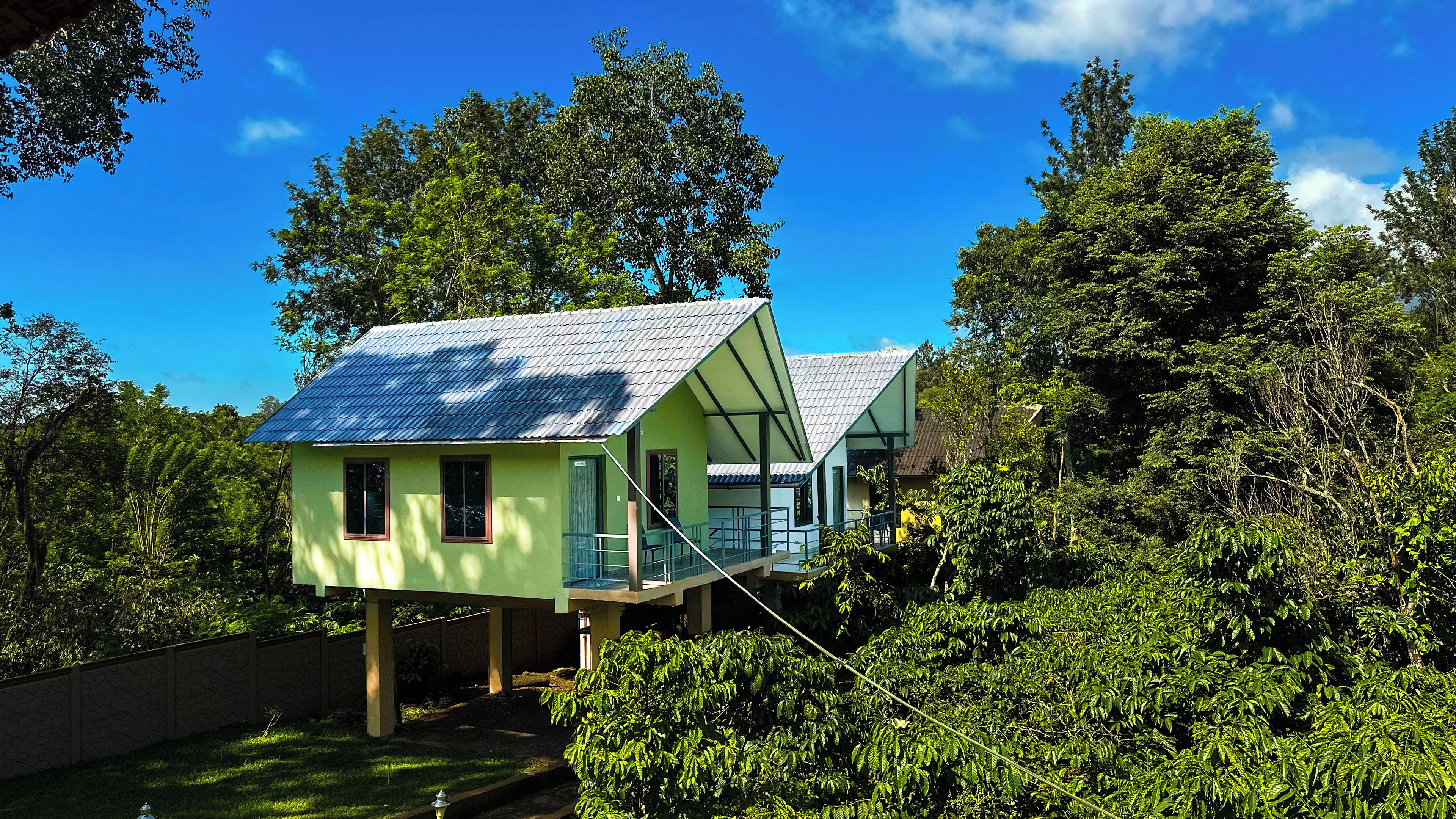 Una casa a due piani con un balcone, immersa nel verde e circondata da alberi.