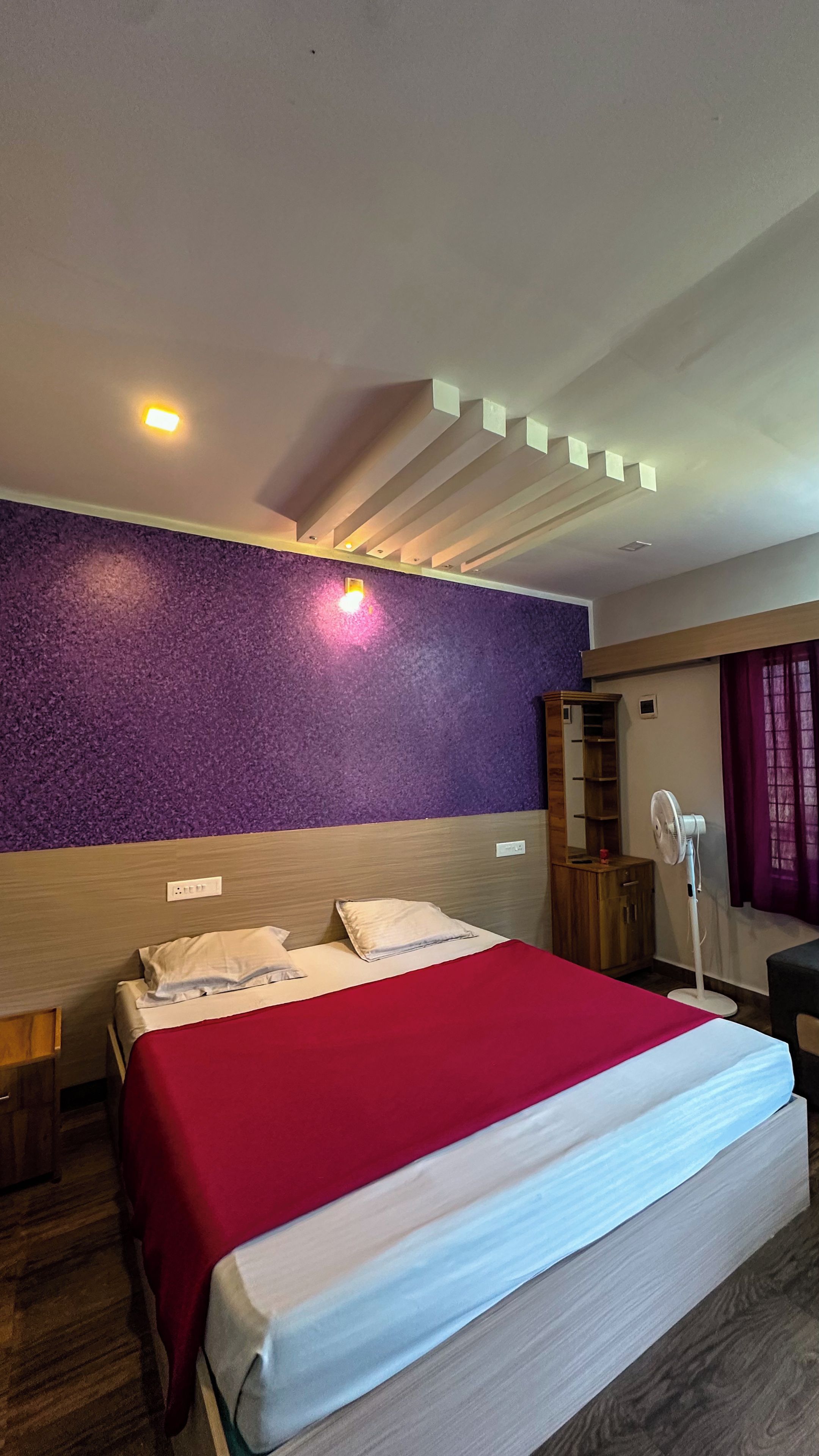 Une chambre d’hôtel avec un grand lit, un mur texturé de couleur violette et un plafond doté d’un éclairage encastré.
