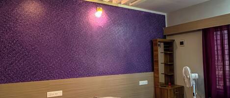 Une chambre d’hôtel avec un grand lit, un mur texturé de couleur violette et un plafond doté d’un éclairage encastré.