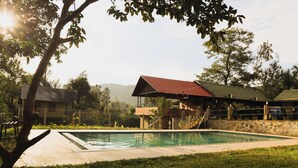 Piscina com muro de pedra e um edifício com telhado vermelho ao fundo.