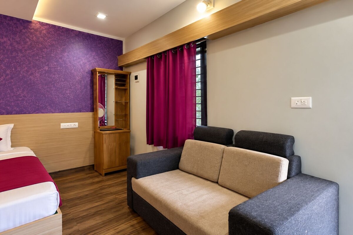Quarto com cama, sofá, guarda-roupa de madeira e janela com cortinas.