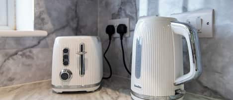 A kitchen counter with a toaster and a kettle, both white, with a marble backsplash and a power outlet in the background.