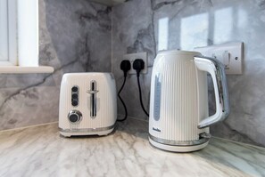 A kitchen counter with a toaster and a kettle, both white, with a marble backsplash and a power outlet in the background. - Chapel Street Flat 3-Perfect for Parks&Recreation (Long Eaton, Nottingham)