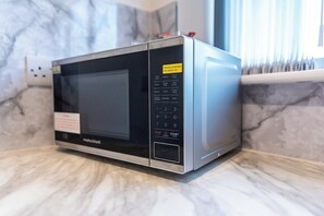 A modern microwave oven with a digital display and control panel, placed on a marble countertop.