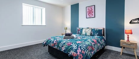 A bedroom with a bed, a window, a nightstand, and a wall-mounted lamp.
