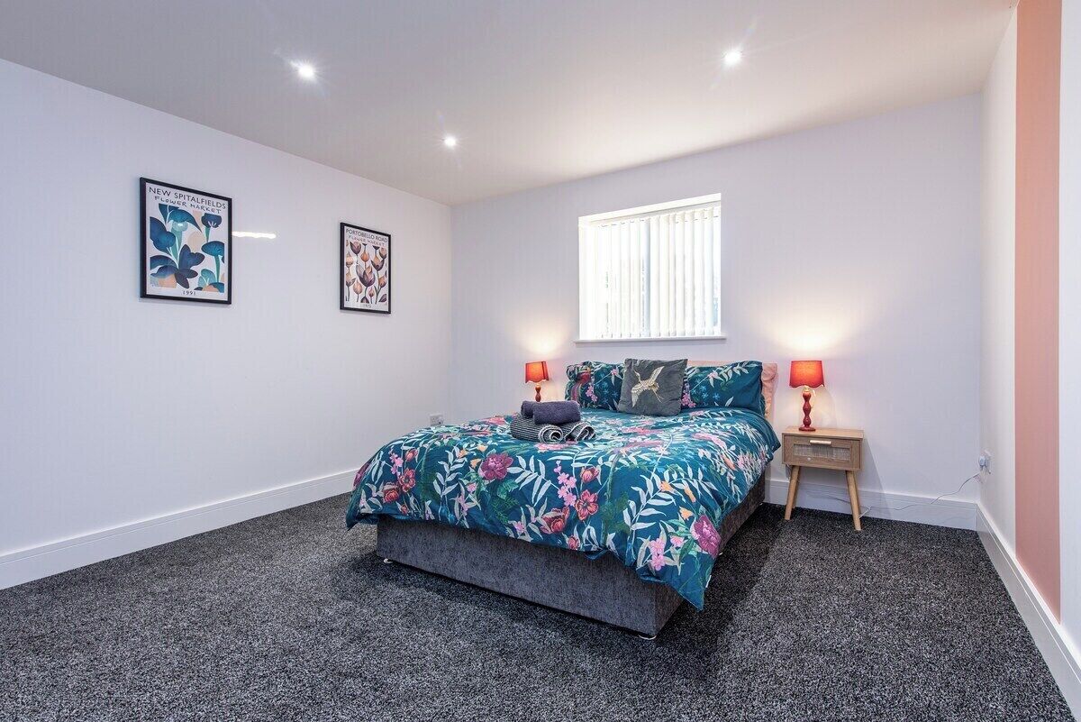 A bedroom with a bed, two wall-mounted lamps, and two framed botanical prints.