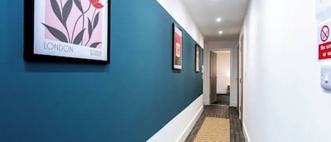 A hallway with teal walls, a wooden floor, and framed artwork.
