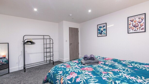 A bedroom with a bunk bed, a bed with a floral duvet, a wall-mounted rack, and two framed pictures. - Chapel Street Flat 5 - Near Nottingham City Centre (Long Eaton, Nottingham)